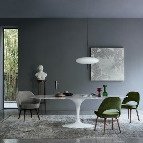 Mid century modern designer white oval dinner table, in a grey wall dining room, with two green chairs and one grey chair