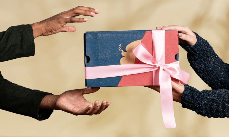 A black man receiving  from a white woman a gift box wrapped in a pink bow containing international coffee